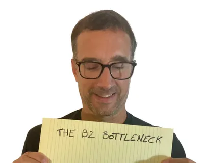 Yann smiling down at a yellow notepad sheet that reads "The B2 bottleneck"