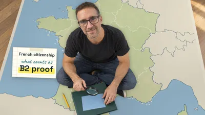 Yann sitting cross-legged on a floor map of France, checking a blank card with a magnifying glass, next to a note that reads "French citizenship, what counts as B2 proof"