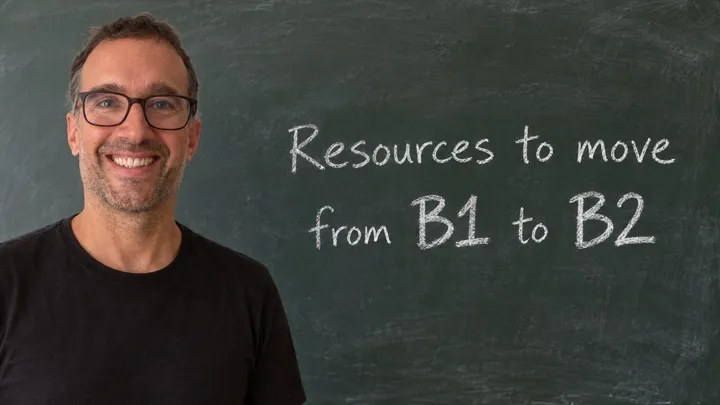 Yann smiling in front of a classroom blackboard that reads "Resources to move from B1 to B2" in white chalk