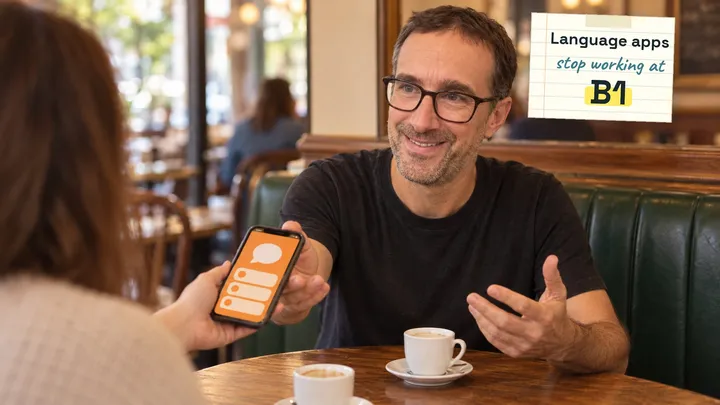 Yann smiling at a brasserie table as the person opposite hands him their phone, a language app on its screen, under a note that reads "Language apps stop working at B1"